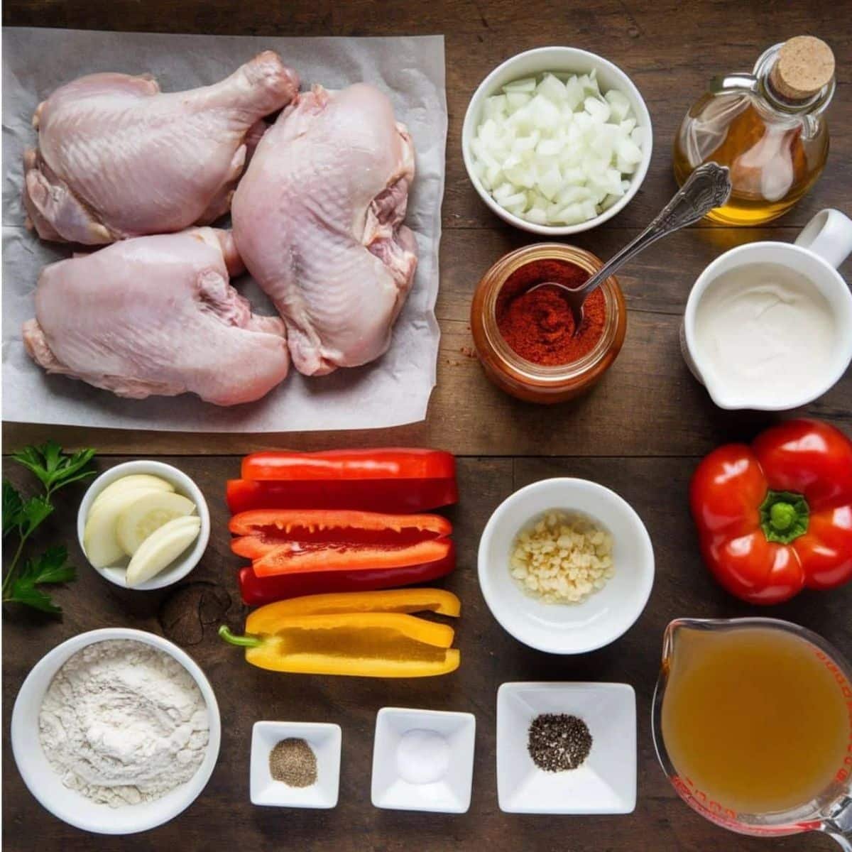 Chicken Paprikash Recipe Ingredients – Raw chicken, paprika, onions, garlic, bell peppers, flour, sour cream, chicken broth, and seasonings on a rustic wooden surface. Essential ingredients for a traditional Hungarian Chicken Paprikash dish.