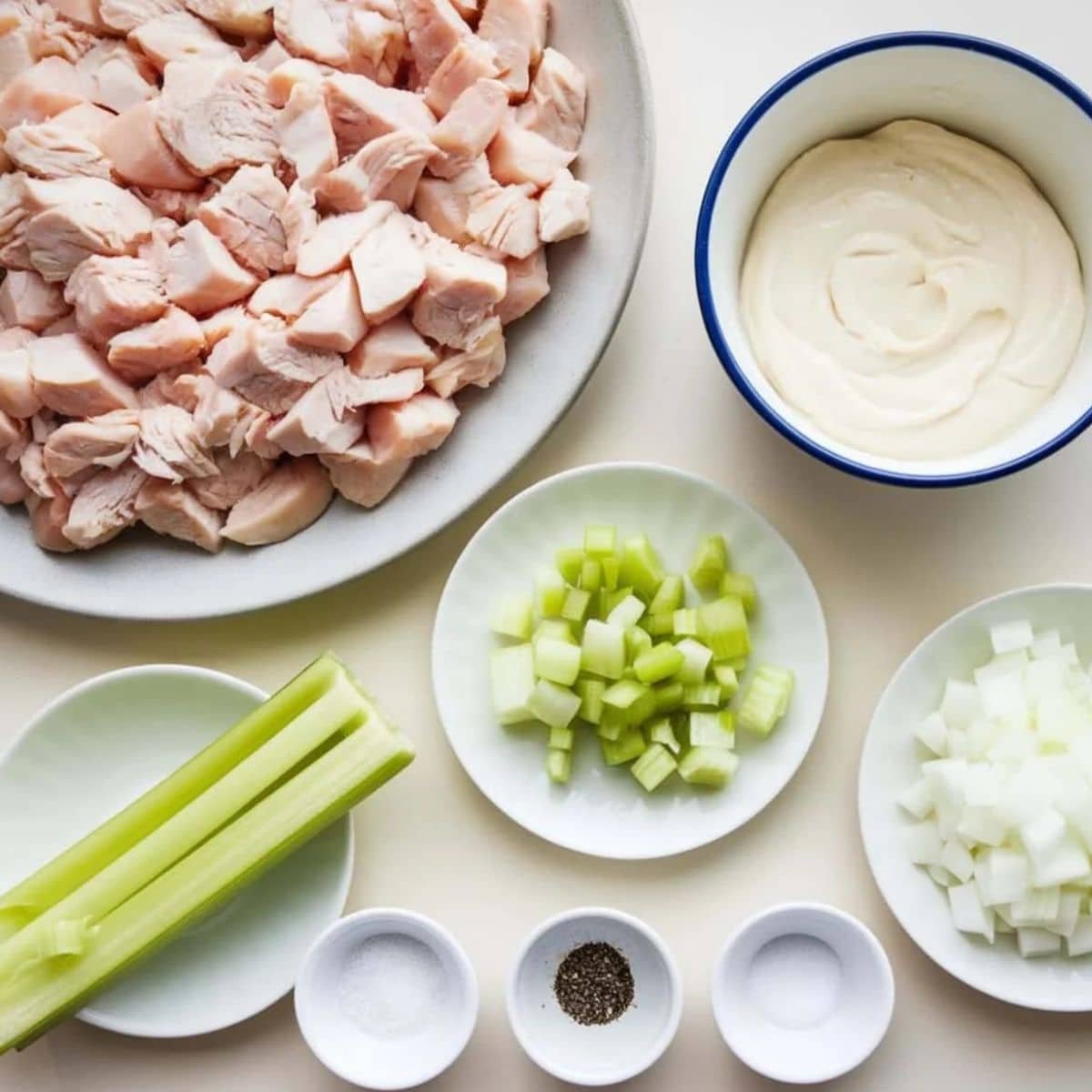 Ingredients for a Chicken Salad Chick recipe, including diced chicken, mayonnaise, chopped celery, onions, and seasoning, neatly arranged on a white surface for a fresh and classic dish.