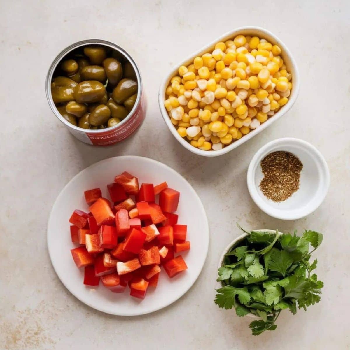 Fresh and zesty ingredients for a Chicken Salad Chick recipe, including diced red bell peppers, canned jalapeños, sweet corn, ground spices, and fresh cilantro on a light background.