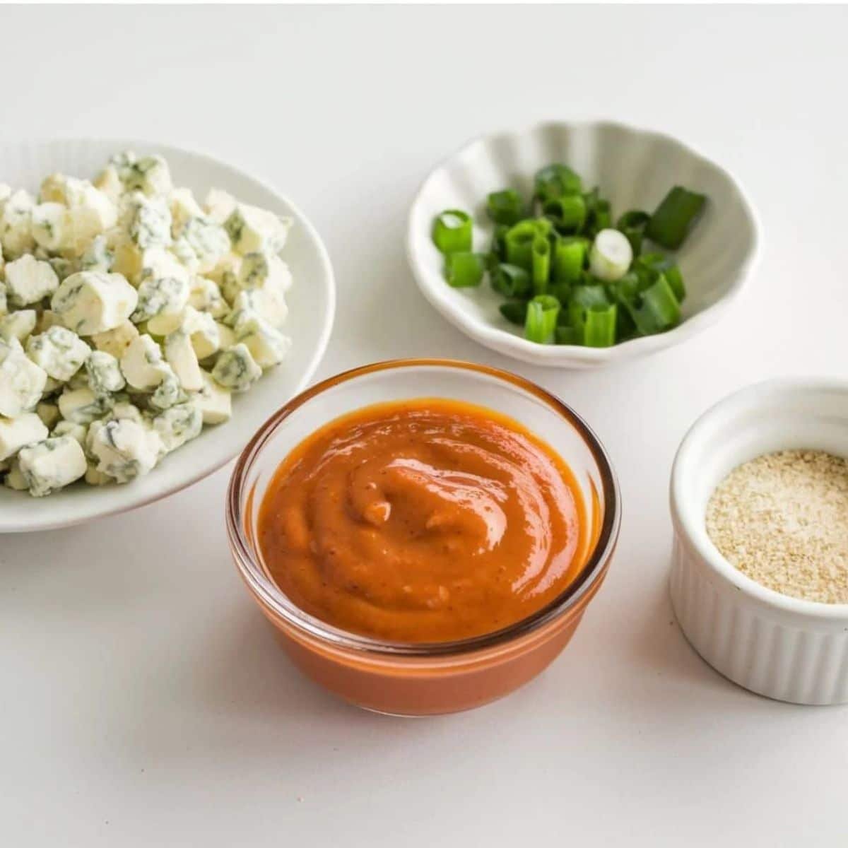 Southwest-inspired ingredients for a Chicken Salad Chick recipe, featuring blue cheese crumbles, sliced green onions, sesame seeds, and a bold, zesty dressing in a glass bowl.