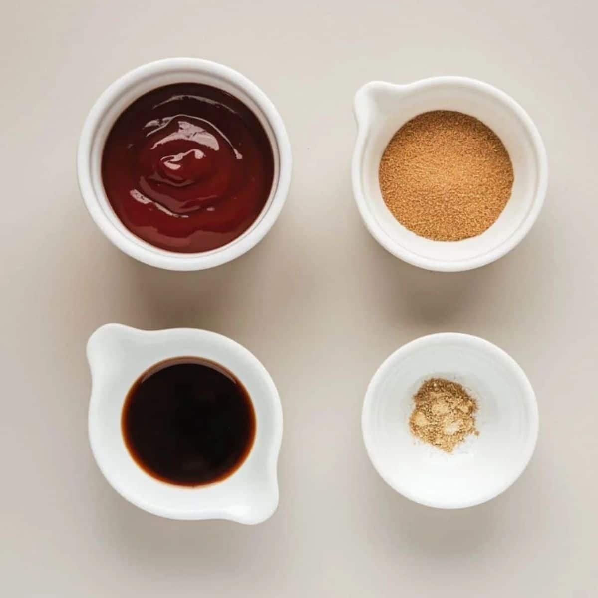 Flavorful glaze ingredients for a meatloaf recipe, including ketchup, brown sugar, Worcestershire sauce, and ground mustard, displayed in small white bowls on a neutral background.