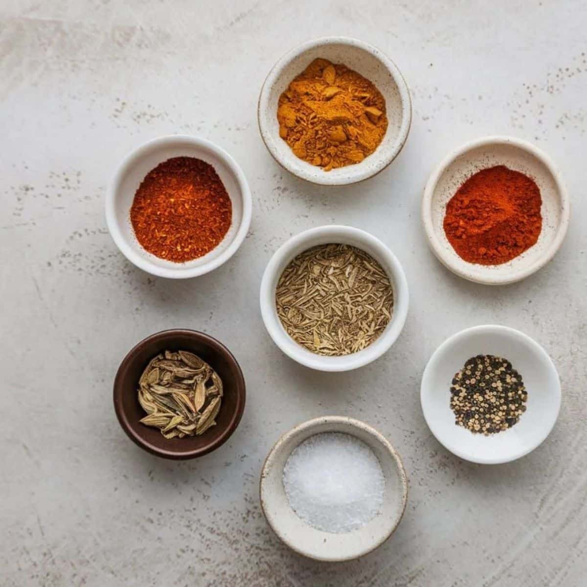 Homemade spice blend for chicken tacos recipe, featuring chili powder, paprika, cumin, garlic powder, onion powder, black pepper, and salt in small bowls.