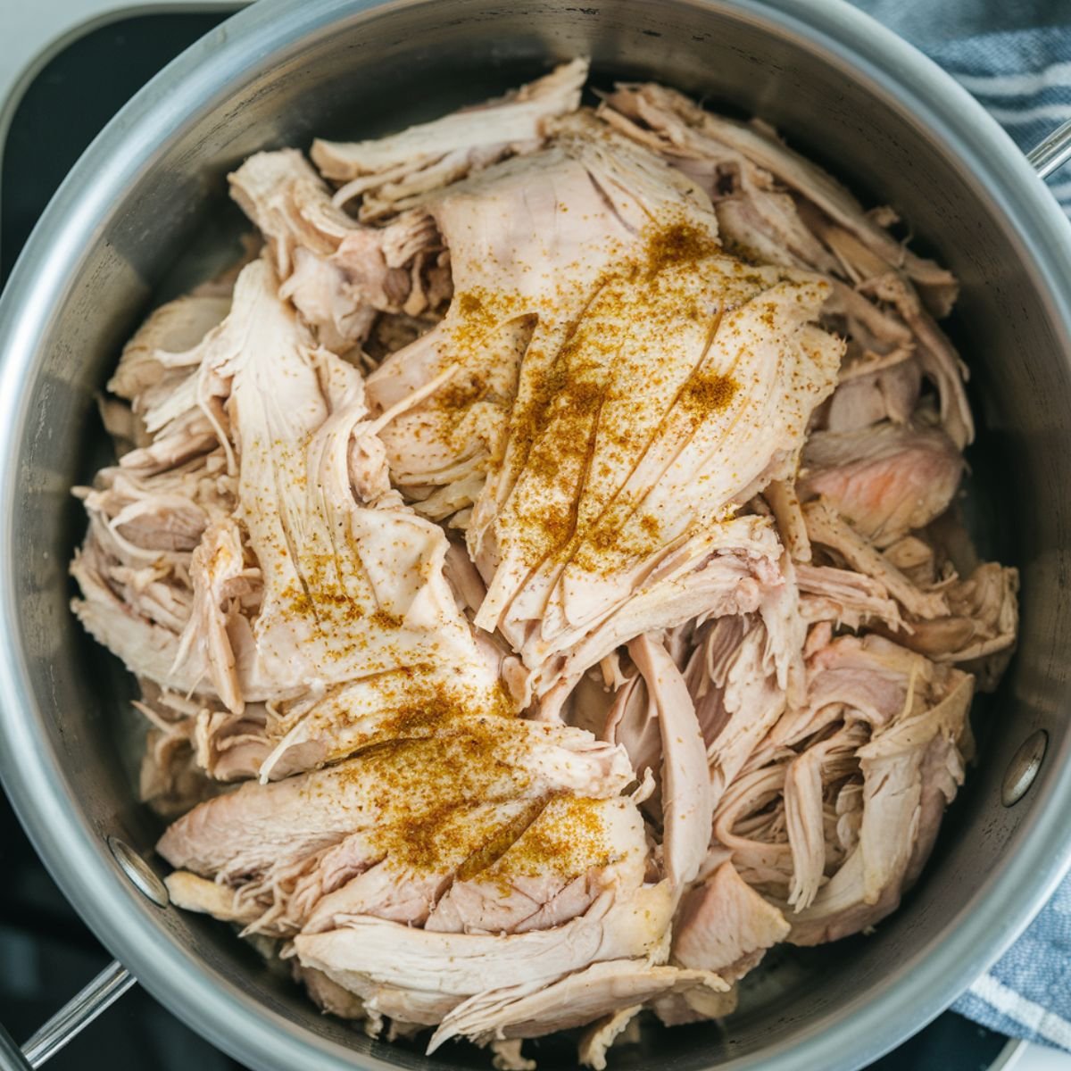 A stainless steel pot filled with Instant Pot Shredded Chicken, tender and juicy with a light seasoning on top. Perfect for meal prep, tacos, sandwiches, or salads. An easy and flavorful recipe made in the Instant Pot.