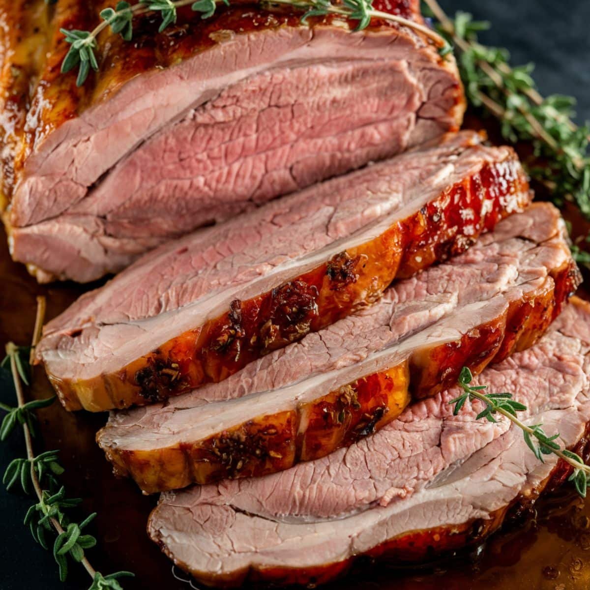 Tender and flavorful smoked pork loin slices with a golden-brown glaze, garnished with fresh thyme, perfect for a smoked pork loin recipe.