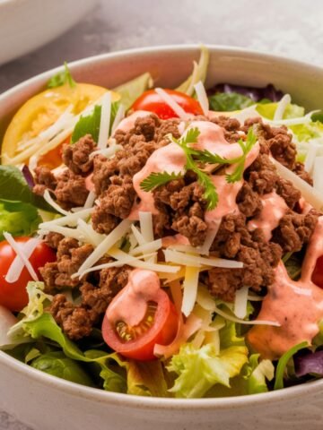 A fresh and vibrant Burger Bowl Recipe featuring seasoned ground beef, crisp lettuce, cherry tomatoes, shredded cheese, and a creamy burger sauce, garnished with fresh cilantro. A healthy, low-carb twist on a classic cheeseburger served in a bowl.