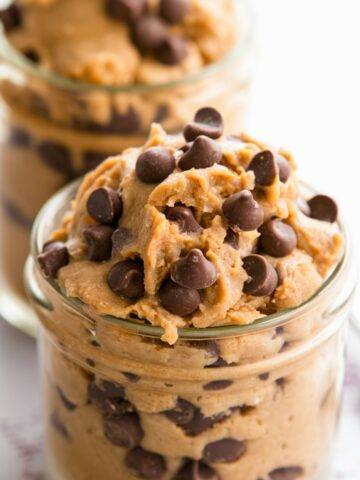 A jar filled with creamy, edible protein cookie dough topped with rich chocolate chips. This high-protein, no-bake dessert is a healthy and indulgent treat, perfect for a nutritious snack. Made with wholesome ingredients like protein powder, nut butter, and natural sweeteners for a guilt-free cookie dough experience.