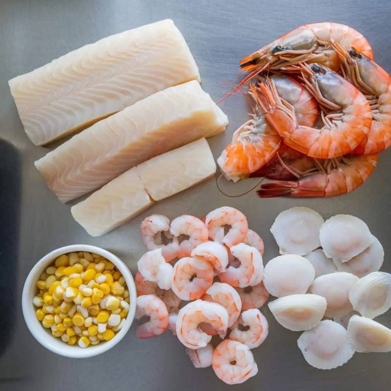 Fresh seafood ingredients for a hearty seafood chowder recipe, including shrimp, scallops, white fish, and sweet corn. A delicious combination for a rich and flavorful homemade chowder.