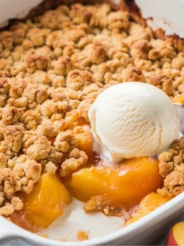 Homemade peach crumble recipe served warm with a scoop of vanilla ice cream. A golden, buttery crumble topping over sweet, baked peaches, making a delicious and comforting dessert.