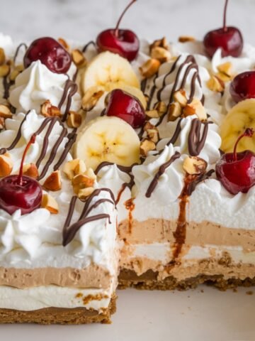 Decadent No-Bake Banana Split Cake Recipe – A layered dessert featuring a crunchy graham cracker crust, creamy banana and chocolate filling, whipped topping, fresh banana slices, maraschino cherries, chopped nuts, and a drizzle of chocolate syrup. A delicious twist on the classic banana split!