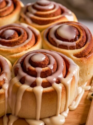 A batch of freshly baked Cake Mix Cinnamon Rolls, golden brown and soft, drizzled generously with sweet vanilla glaze. The rolls are placed on a wooden board with a butter knife nearby, creating a cozy and inviting homemade dessert scene.