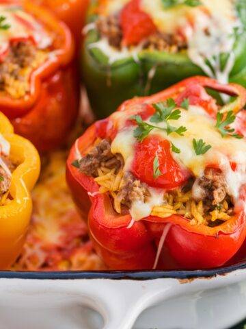 Old Fashioned Stuffed Bell Peppers Recipe featuring vibrant red, yellow, and green bell peppers filled with a savory mixture of ground beef, rice, and tomato sauce, topped with melted cheese and garnished with fresh parsley. Baked in a white casserole dish, this classic comfort food is rich, hearty, and full of flavor.