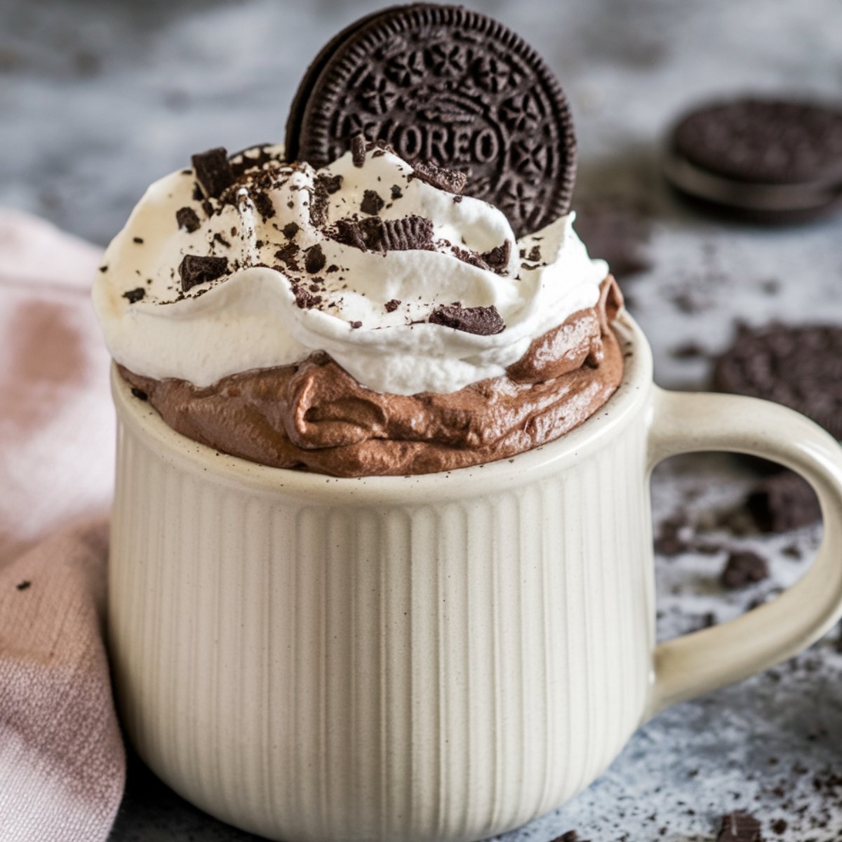 A rich and chocolatey Oreo mug cake recipe topped with fluffy whipped cream, crushed Oreo pieces, and a whole Oreo cookie, served in a ribbed ceramic mug. A quick and easy dessert made in minutes with simple ingredients.