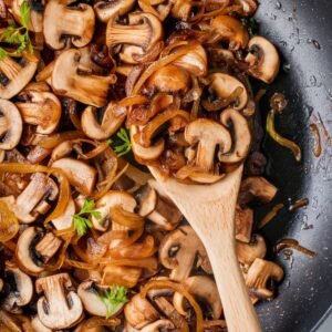 close-up of sautéed mushrooms and onions in a skillet, glistening in melted butter. This rich and flavorful mixture is an essential component of a Salisbury steak recipe, used to create a savory mushroom gravy that pairs perfectly with the tender steak patties.