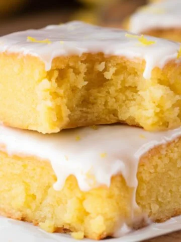 A close-up of delicious Lemon Brownies recipe ,featuring a soft, chewy texture and topped with a sweet, tangy lemon glaze. The bright yellow color and moist crumb highlight the fresh citrus flavor, with a bite taken out to reveal the fudgy interior. Garnished with fresh lemon zest, these lemon brownies are a perfect dessert for citrus lovers.