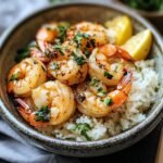 A bowl of homemade Hawaiian garlic shrimp Recipe, glistening with golden garlic butter, lightly charred, and topped with chopped parsley. A lemon wedge sits on the side, with crispy garlic bits clinging to the shrimp. Served in a rustic dish on a cozy dinner table.