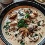 Homemade creamy mushroom soup in a black bowl, topped with parsley and black pepper, with sliced mushrooms in a thick beige broth.