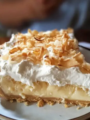 Homemade coconut cream meringue pie slice with golden crust, creamy coconut filling, fluffy meringue, and toasted coconut flakes on top.