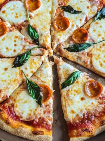 Homemade Margarita Pizza with melted mozzarella, basil leaves, and a few pepperoni slices in a cardboard box.