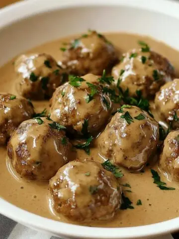 Homemade Swedish meatballs in creamy brown gravy, topped with fresh parsley, served in a white bowl.