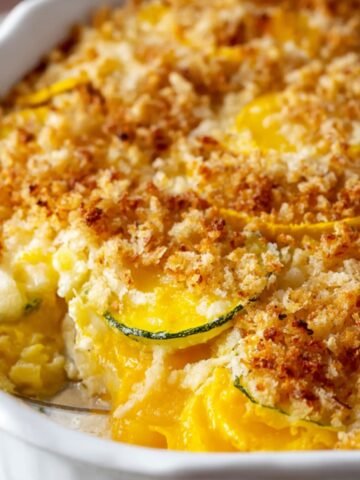 Homemade squash casserole in a white dish with golden breadcrumb topping and a creamy, cheesy squash filling. A portion has been scooped out.