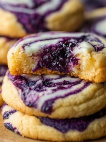 Close-up of homemade blueberry cheesecake swirl cookies with golden edges and rich purple blueberry filling, one cookie partially bitten to reveal a soft, moist center.