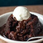 Homemade chocolate pudding cake with a gooey molten center, topped with a scoop of vanilla ice cream in a white bowl.
