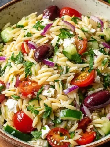 Homemade Greek orzo salad with cherry tomatoes, cucumber, red onion, Kalamata olives, feta cheese, and parsley in a rustic bowl, lightly dressed with olive oil.