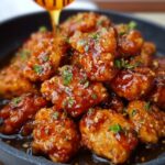 Homemade Honey Butter Chicken glazed in sticky sauce, topped with parsley and sesame seeds, with honey being drizzled over.