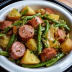 Homemade Kielbasa Green Beans and Potatoes, baby potatoes, and green beans, tossed with onions and herbs, served in a white dish with a black rim.
