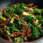 Chinese Beef and Broccoli over white rice in a dark bowl, with tender beef in glossy brown sauce, vibrant broccoli, and green onion garnish, natural light.