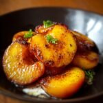 Homemade Pan Fried Peaches, golden and caramelized with crisp edges, glistening in a buttery glaze and garnished with fresh green herbs.