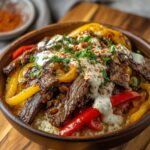 Homemade Philly cheesesteak bowl with cauliflower rice, seared steak, sautéed peppers and onions, creamy white sauce, parsley, and paprika in a wooden bowl.