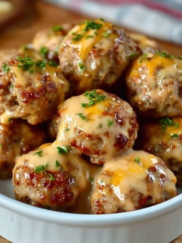 Homemade Rotel Cream Cheese Sausage Balls stacked in a white dish on a wooden board, golden brown with melted cheddar and parsley, dipping sauce in background.