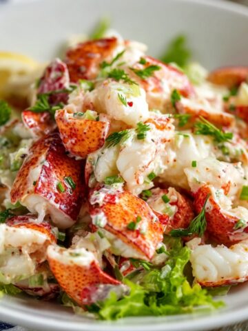 Homemade lobster salad with chunky lobster meat tossed in creamy dressing, fresh herbs, and celery, served on crisp lettuce with a lemon wedge.