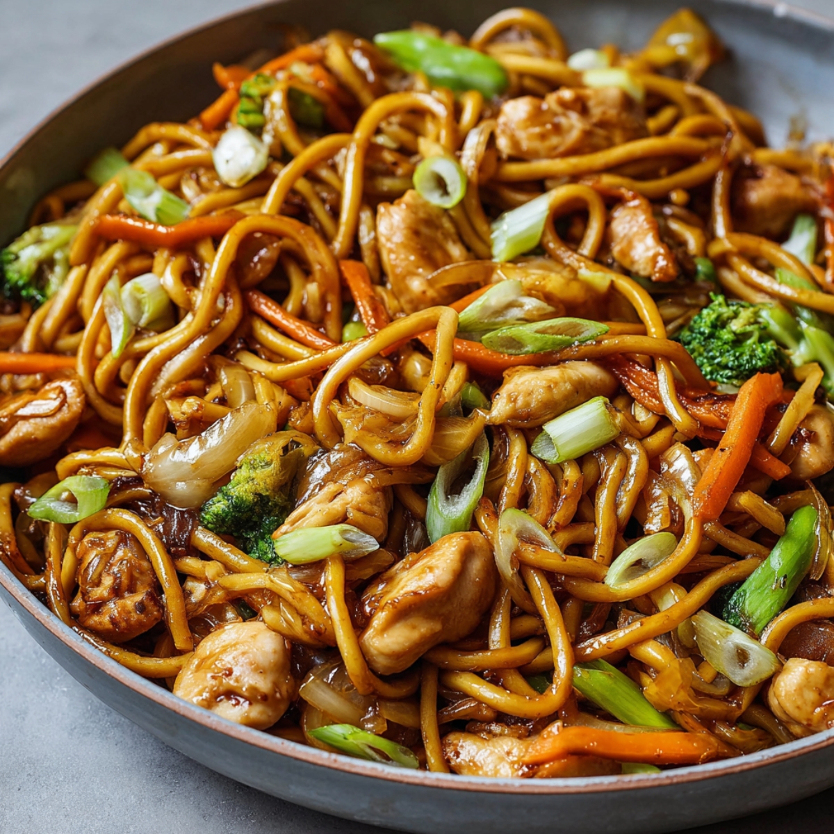 Chicken Lo Mein Recipe in a skillet with glossy noodles, tender chicken pieces, broccoli florets, carrots, onions, and scallions tossed in a rich soy-based sauce — perfectly caramelized and ready to serve, showing real home-cooked texture and freshness.