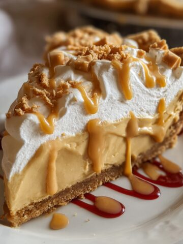 Homemade Butterscotch Heaven Pie with creamy filling, whipped cream, caramel drizzle, and toffee bits on a white plate with caramel and red syrup.
