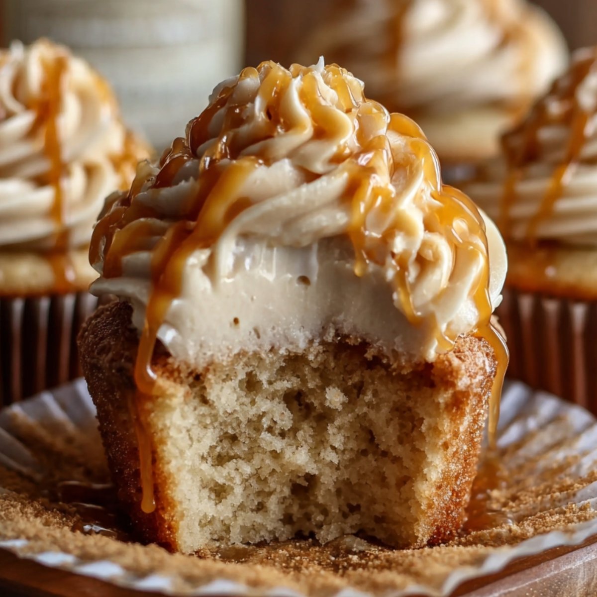 Homemade Harry Potter butterbeer cupcakes with creamy caramel-drizzled frosting, one bitten to show soft, fluffy inside, resting on a book with more cupcakes blurred in the background under warm, cozy lighting.
