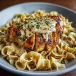Chicken with Buttered Noodles topped with creamy sauce and parsley, served in a gray bowl.