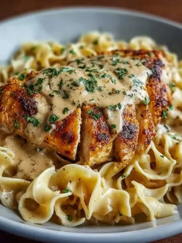 Chicken with Buttered Noodles topped with creamy sauce and parsley, served in a gray bowl.