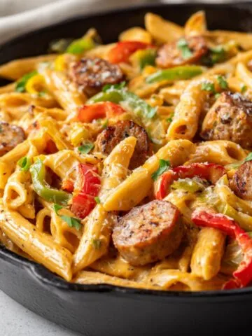 Homemade Creamy Cajun Sausage Pasta in a cast iron skillet with penne, sliced sausage, and colorful bell peppers, topped with herbs and parmesan.