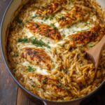 Creamy French onion chicken orzo baked in a skillet, with golden seared chicken thighs, caramelized onions, melted cheese, and fresh thyme on top.