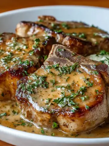 Homemade crock pot pork chops topped with creamy herb gravy and fresh thyme, served on a blue plate.
