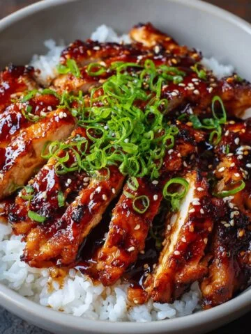 Homemade teriyaki chicken served over steamed white rice, glazed with a glossy soy-ginger sauce and topped with sesame seeds and sliced green onions.