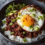 Korean Ground Beef Bowl served over white rice, topped with a sunny-side-up egg, sesame seeds, chopped green onions, and steamed broccoli on the side.