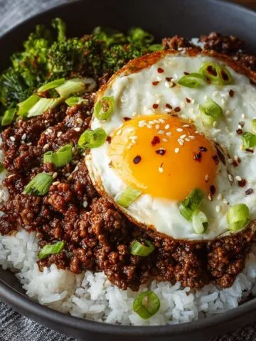 Korean Ground Beef Bowl served over white rice, topped with a sunny-side-up egg, sesame seeds, chopped green onions, and steamed broccoli on the side.