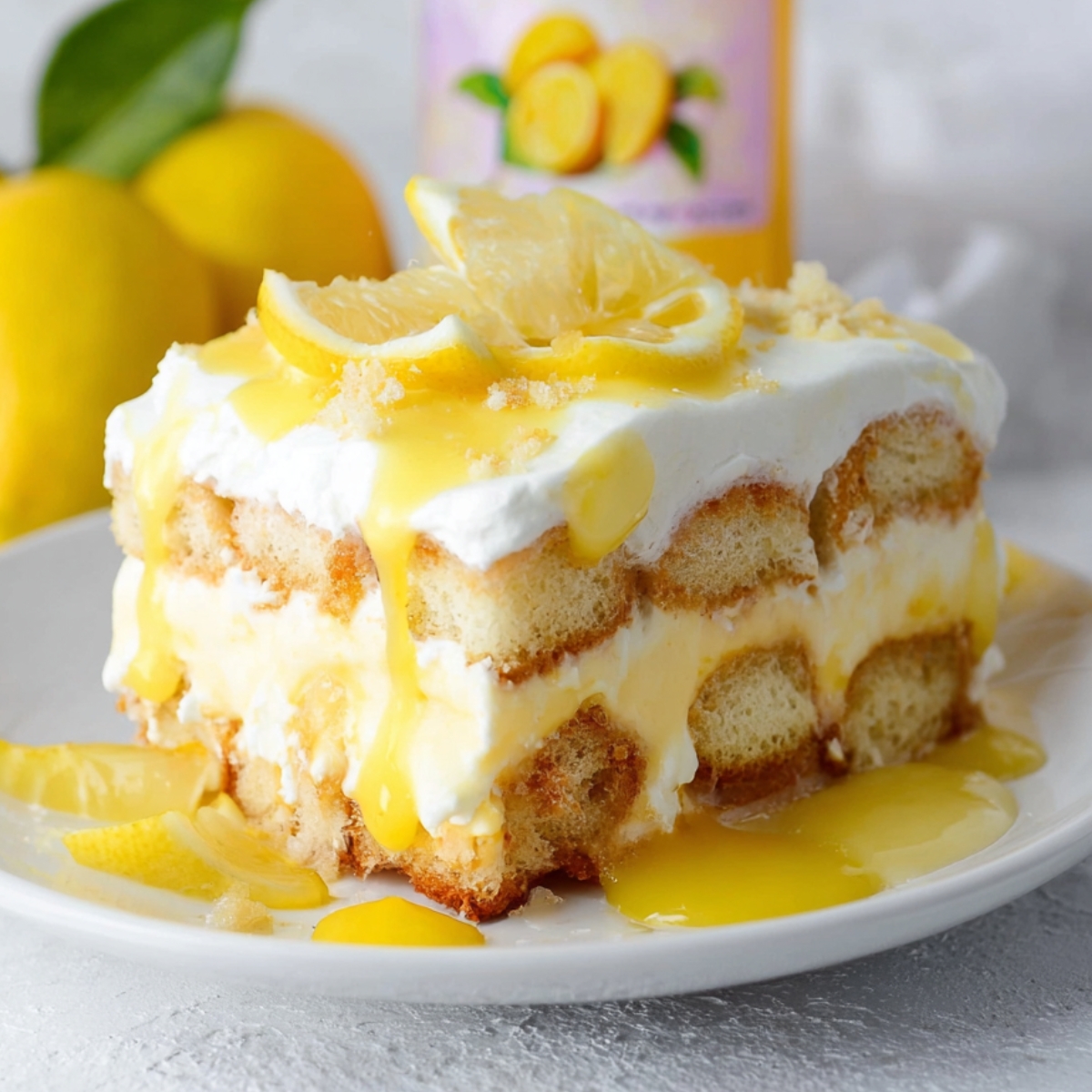 A homemade slice of lemon tiramisu with layers of ladyfingers, lemon cream, whipped topping, and lemon curd dripping down the sides, topped with fresh lemon slices on a white plate.