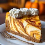 Pumpkin Swirl Cheesecake with a crumb crust and whipped cream on top, served on a white plate.