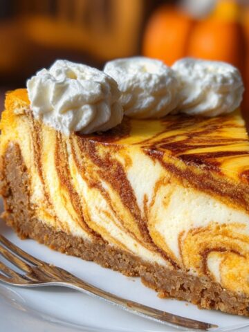Pumpkin Swirl Cheesecake with a crumb crust and whipped cream on top, served on a white plate.