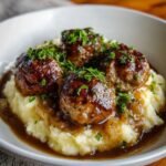 Homemade Salisbury steak meatballs served over creamy mashed potatoes with rich onion gravy and fresh parsley on top.