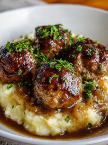 Homemade Salisbury steak meatballs served over creamy mashed potatoes with rich onion gravy and fresh parsley on top.